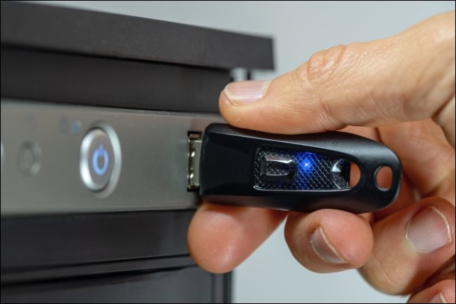 Dłoń wkładająca pamięć flash USB do komputera stacjonarnego.
