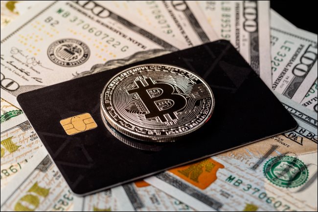 Un jeton Bitcoin physique au-dessus d'une carte de crédit posée sur des billets de 100 $.