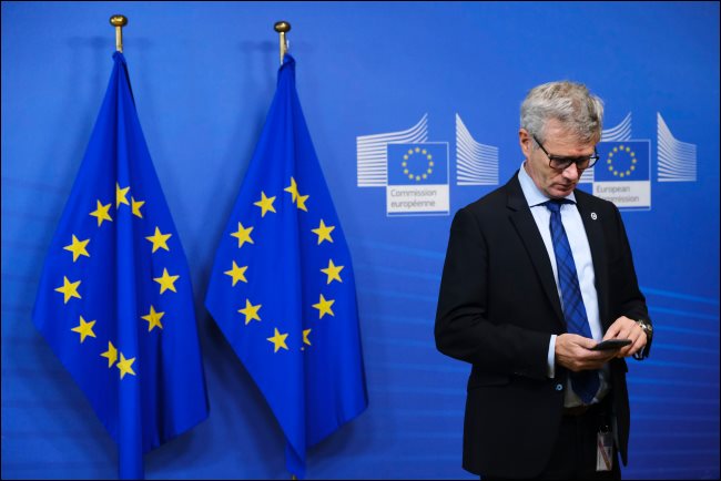 Un hombre que usa un teléfono inteligente con dos banderas de la UE detrás de él.