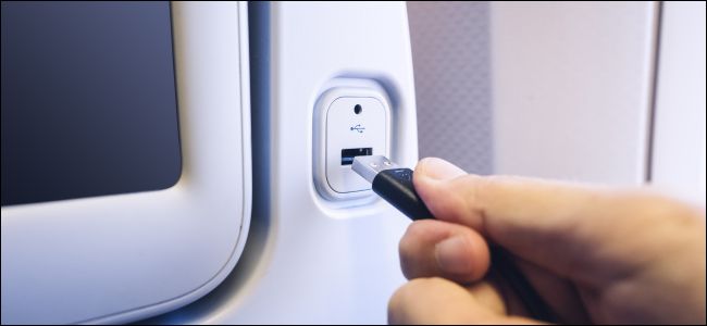 Une main branchant un cordon USB dans un port de charge à l'arrière d'un siège d'avion.